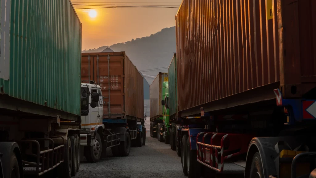Camiones con contenedores alineados en una terminal logística al atardecer